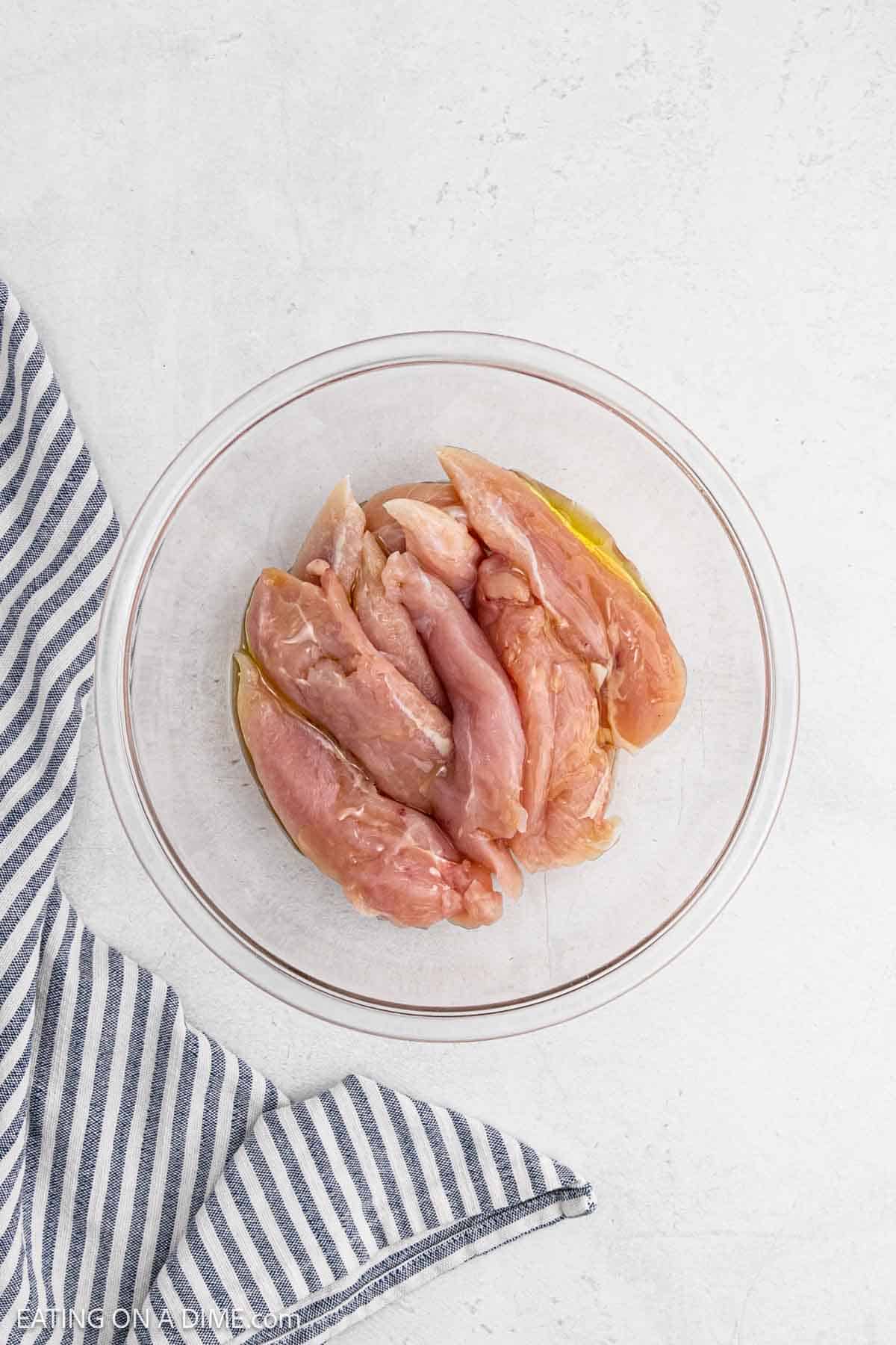 Raw chicken tenderloins in a bowl with oil.