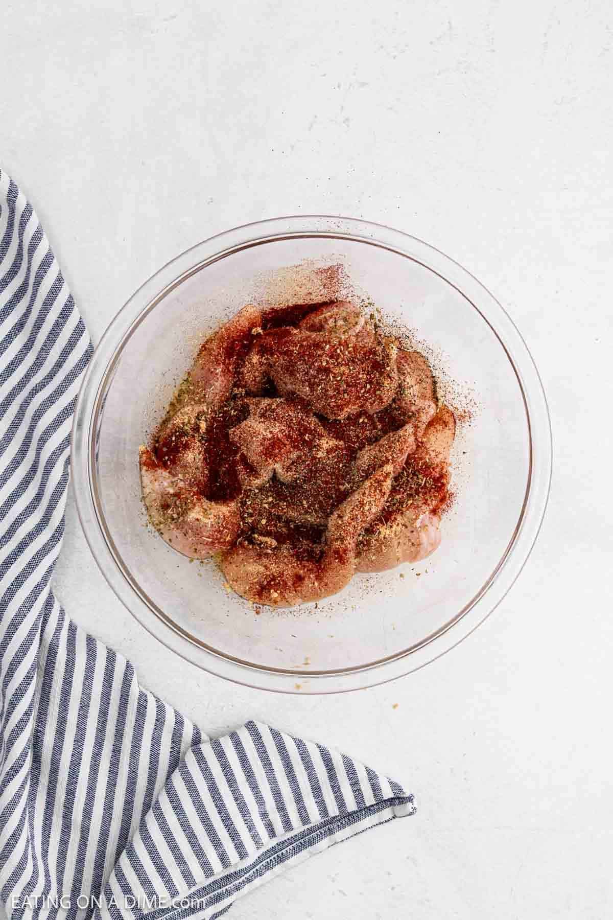 Seasoning blend sprinkled over the raw chicken tenderloin in the bowl with oil.