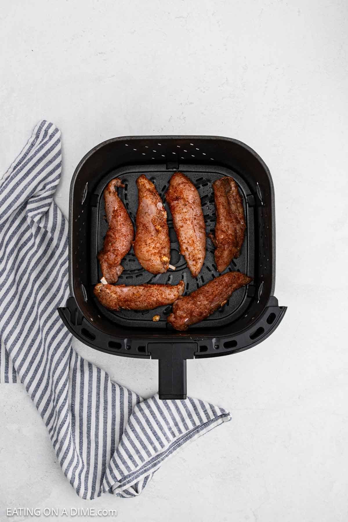 Seasoned raw chicken tenderloins in the air fryer basket.