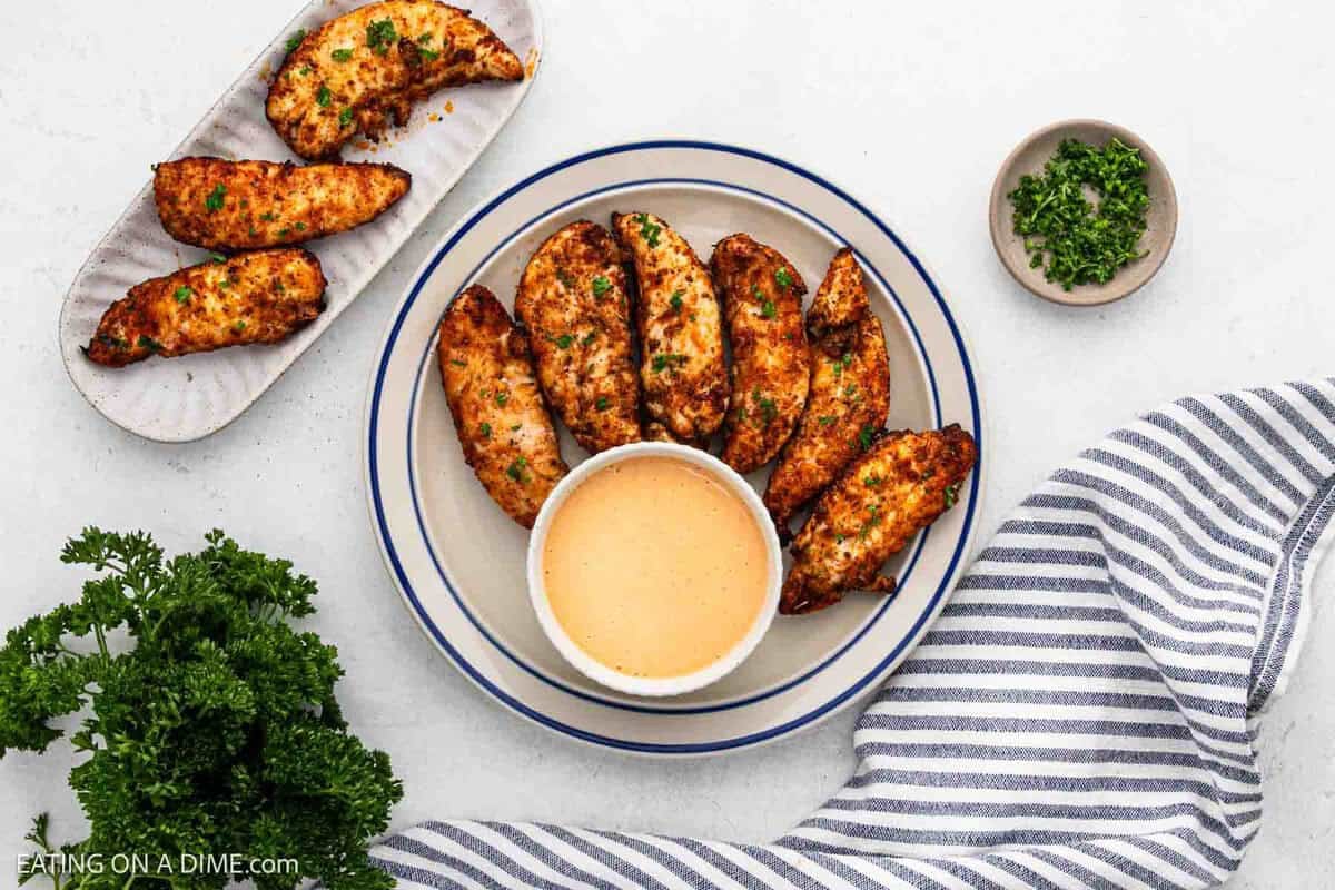 Air Fryer Chicken Tenderloins on a plate and platter with a bowl of dipping sauce on the side.