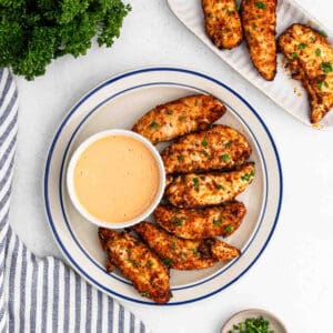 Cooked chicken tenderloins on a plate with a side of honey mustard in a bowl.