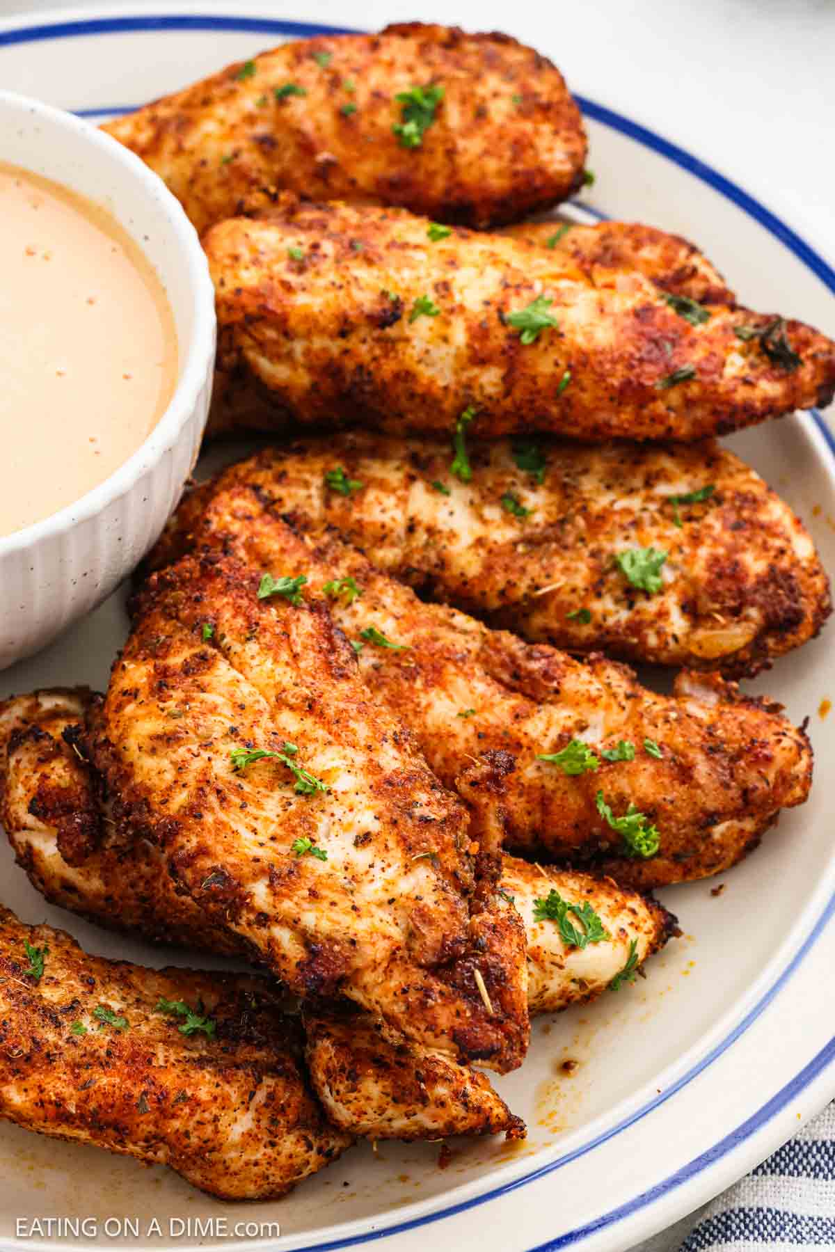 Cooked chicken tenders stacked on a platter with a bowl of sauce nearby.