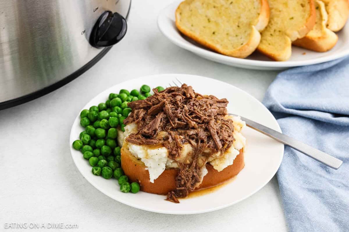 Beef Manhattan on a plate with a side of peas and a plate of garlic toast nearby.
