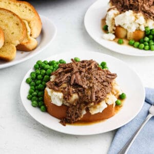 A serving of Beef Manhattan on a plate with a side of green peas.