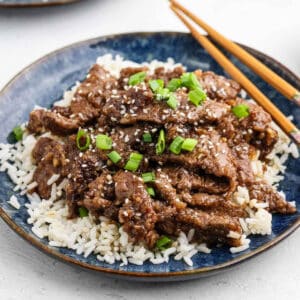 Beef Teriyaki on a plate of white rice topped with green onions and sesame seeds.