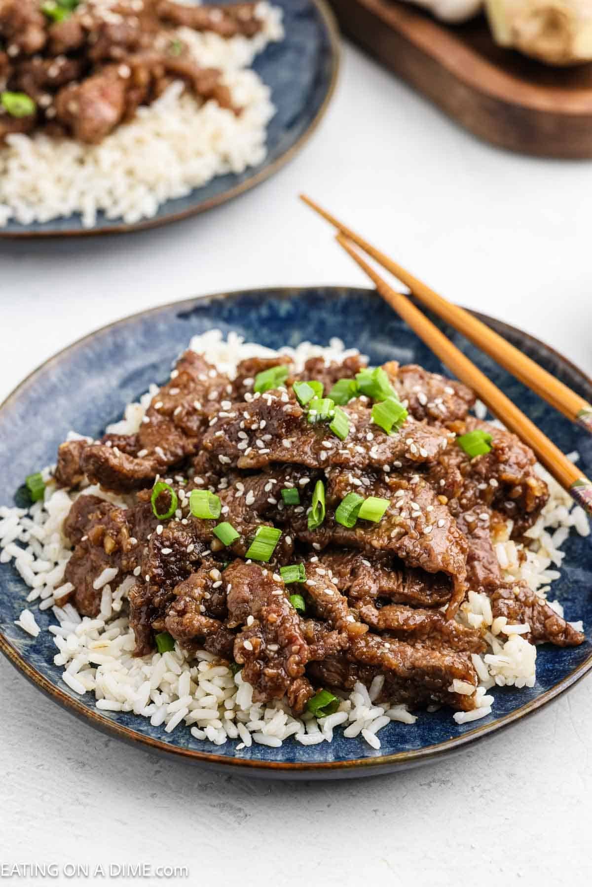 Teriyaki beef over rice on a plate topped with green onions and sesame seeds.