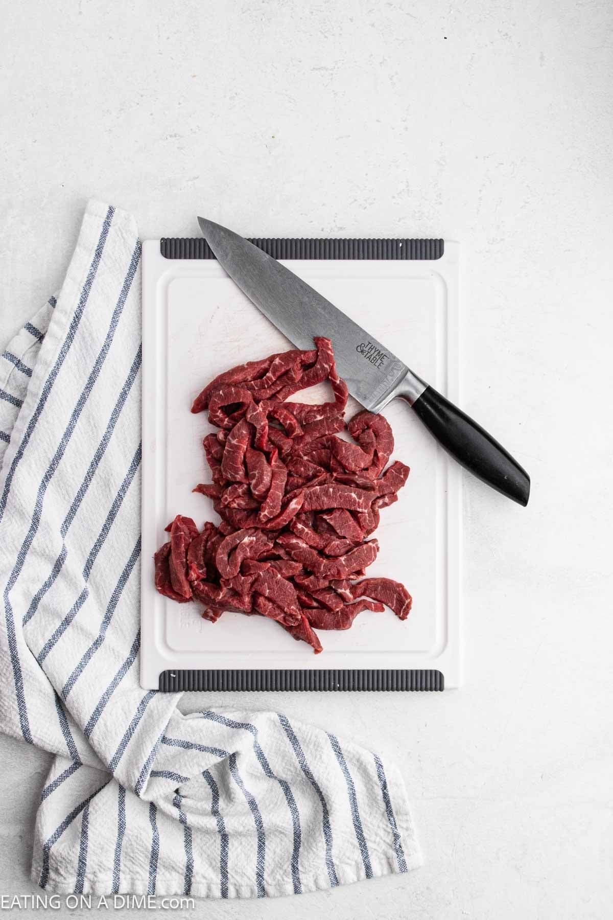 Slicing flank steak into strips on a cutting board with a knife.