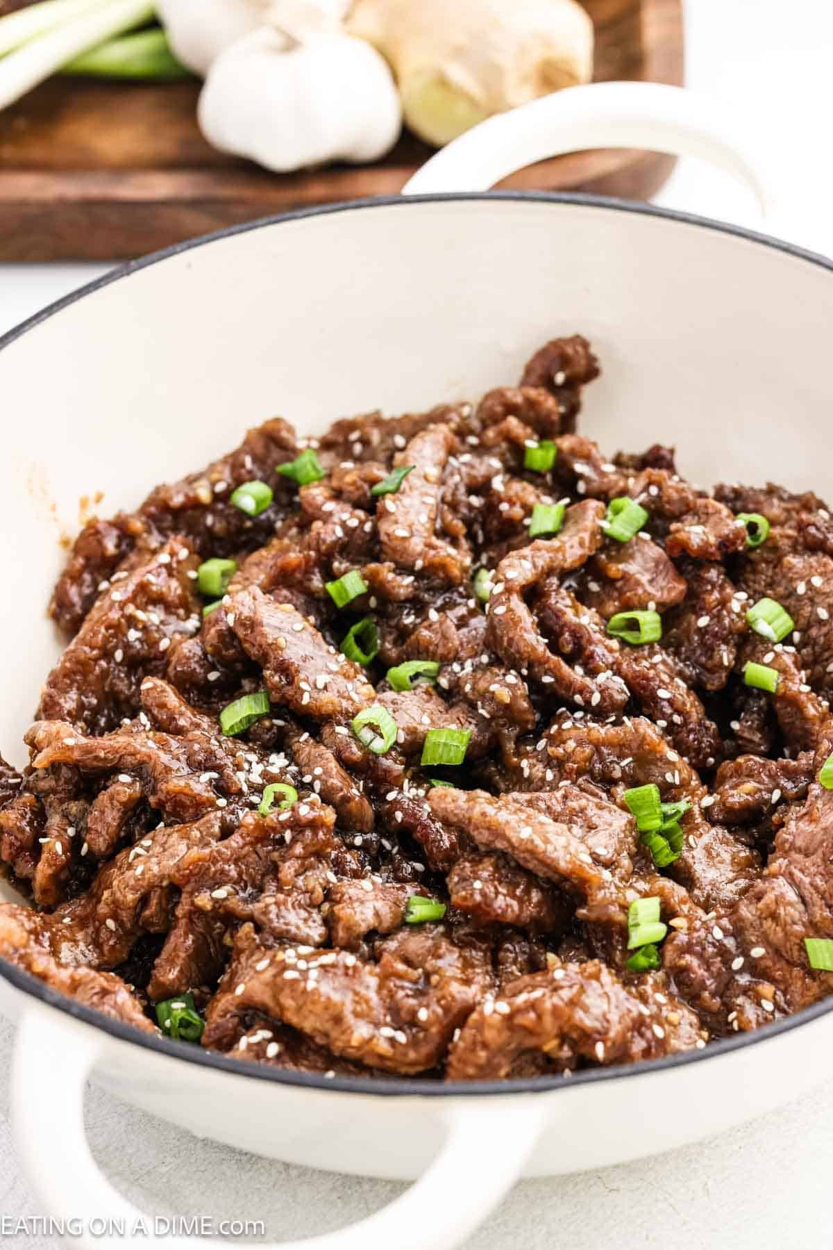 Teriyaki steak in a large pot topped with green onions and sesame seeds.