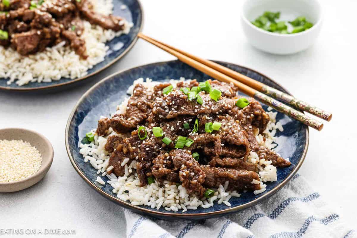 Beef teriyaki over rice on a plate topped with green onions and sesame seeds.
