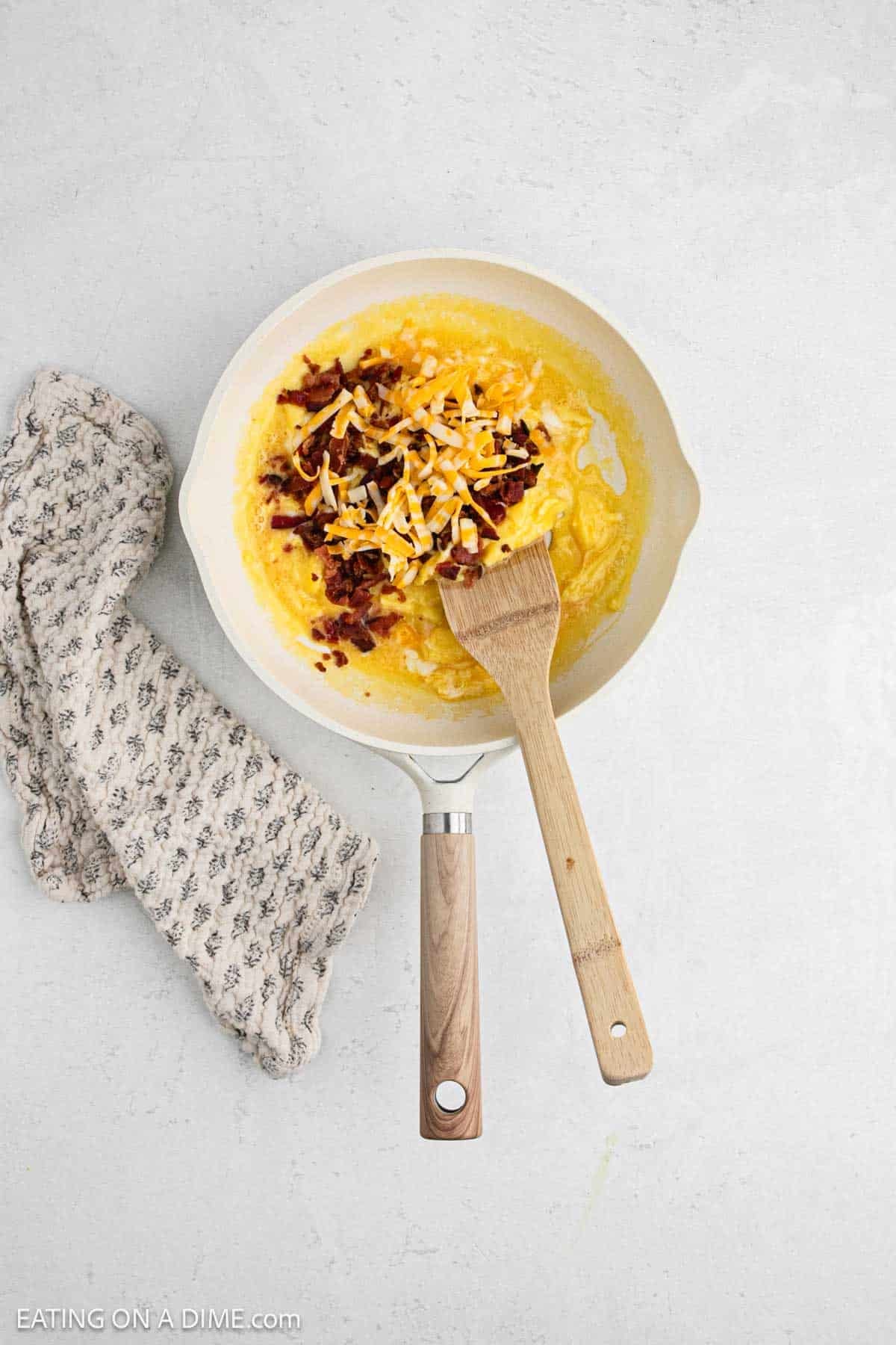 Eggs added to a skillet topped with cheese and crispy bacon.