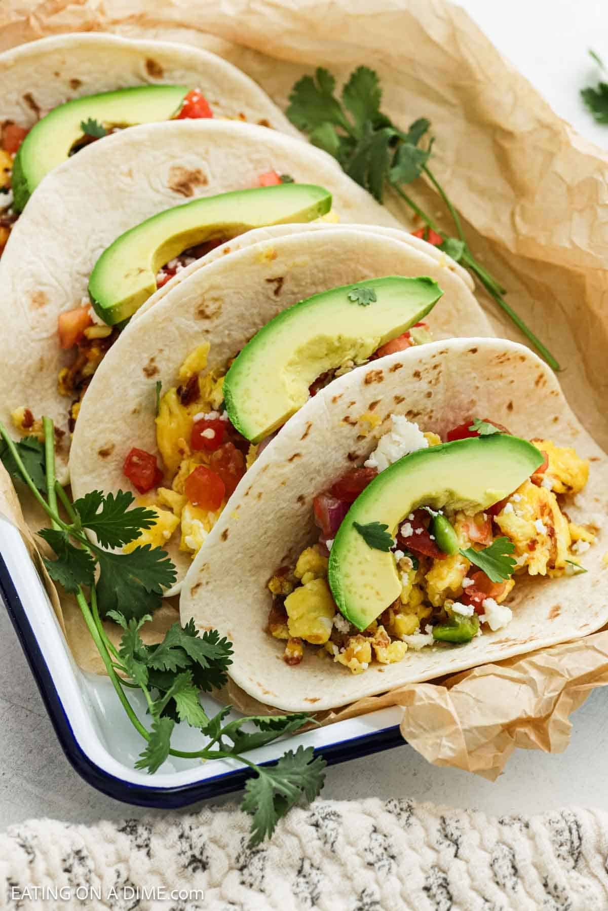 Tortillas filled with eggs and crispy bacon topped with slice avocado on a tray.