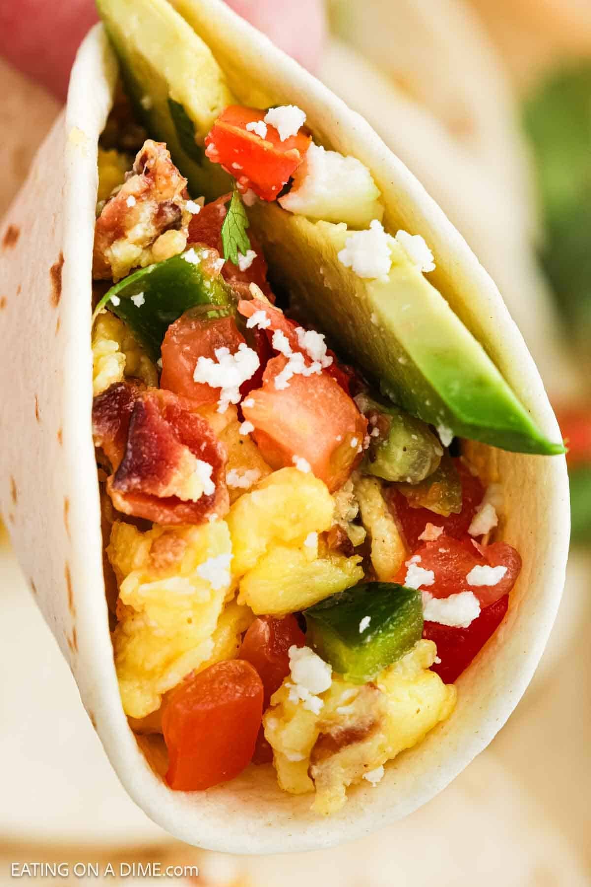 Close up image of eggs, crispy bacon, and veggies all wrapped in a tortilla.