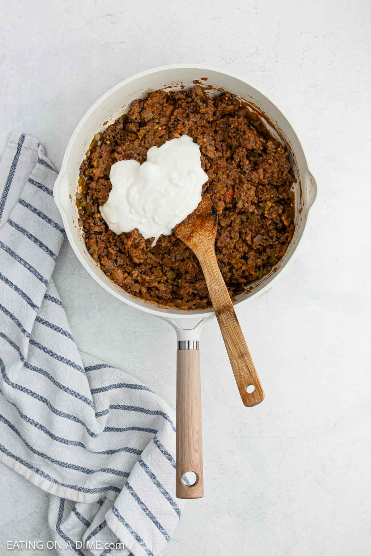 Cooked ground beef mixed with taco seasoning in a skillet topped with sour cream.