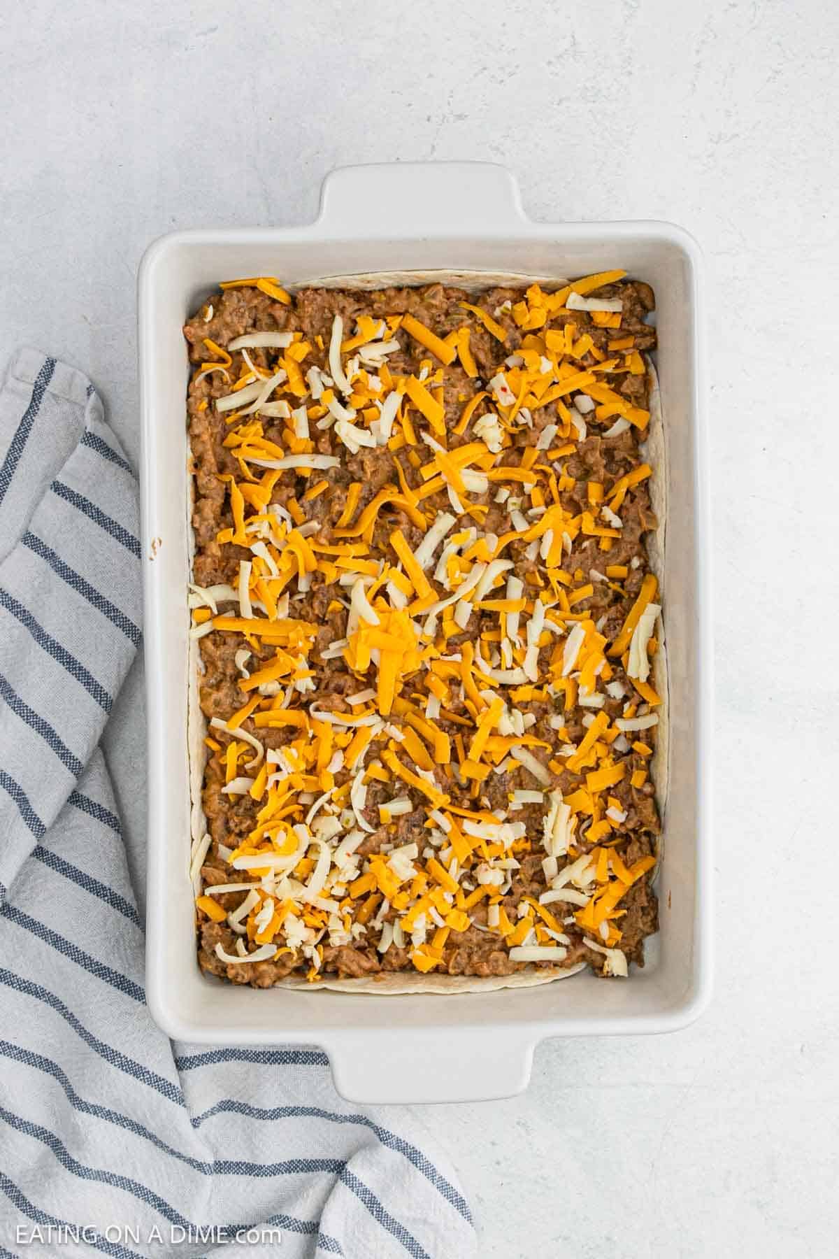Meat mixture spread over the tortillas in a baking dish topped with shredded cheese.