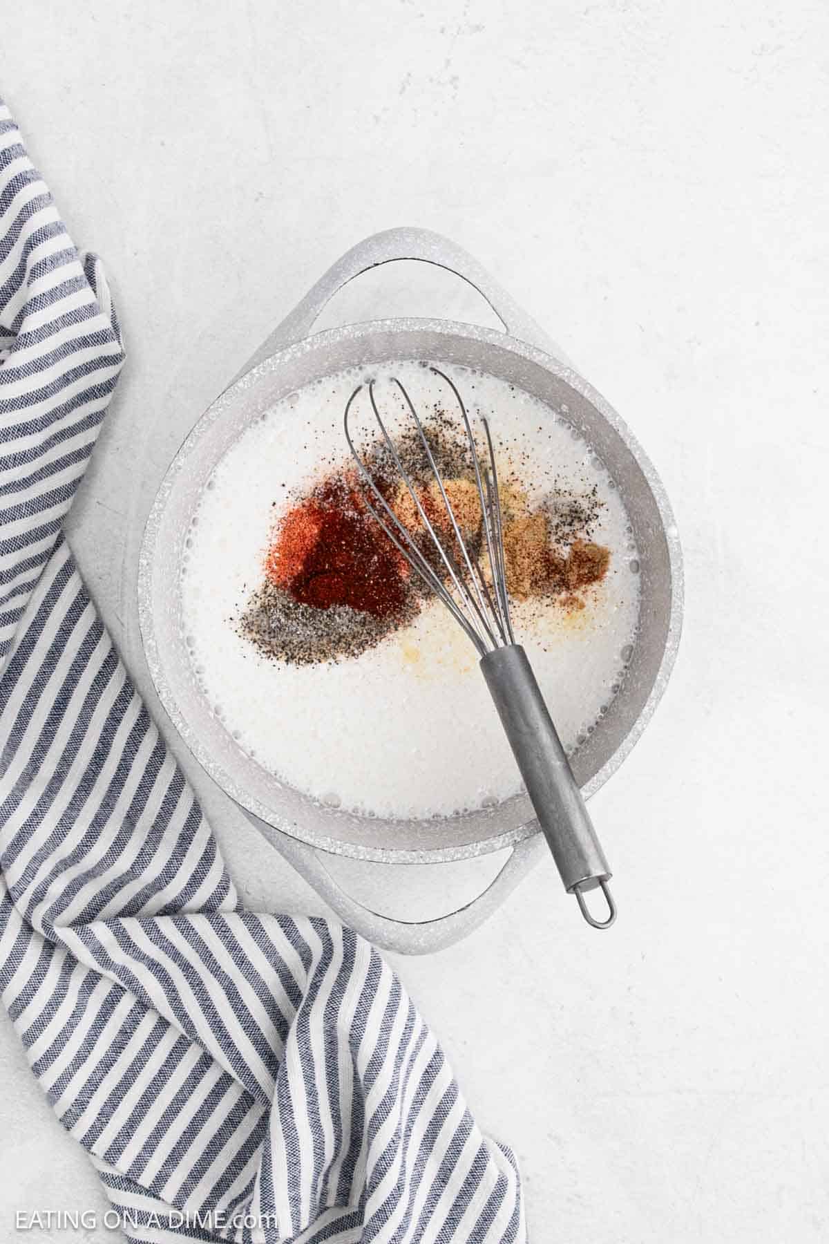Combining the spices into the milk mixture in a large pot with a whisk.