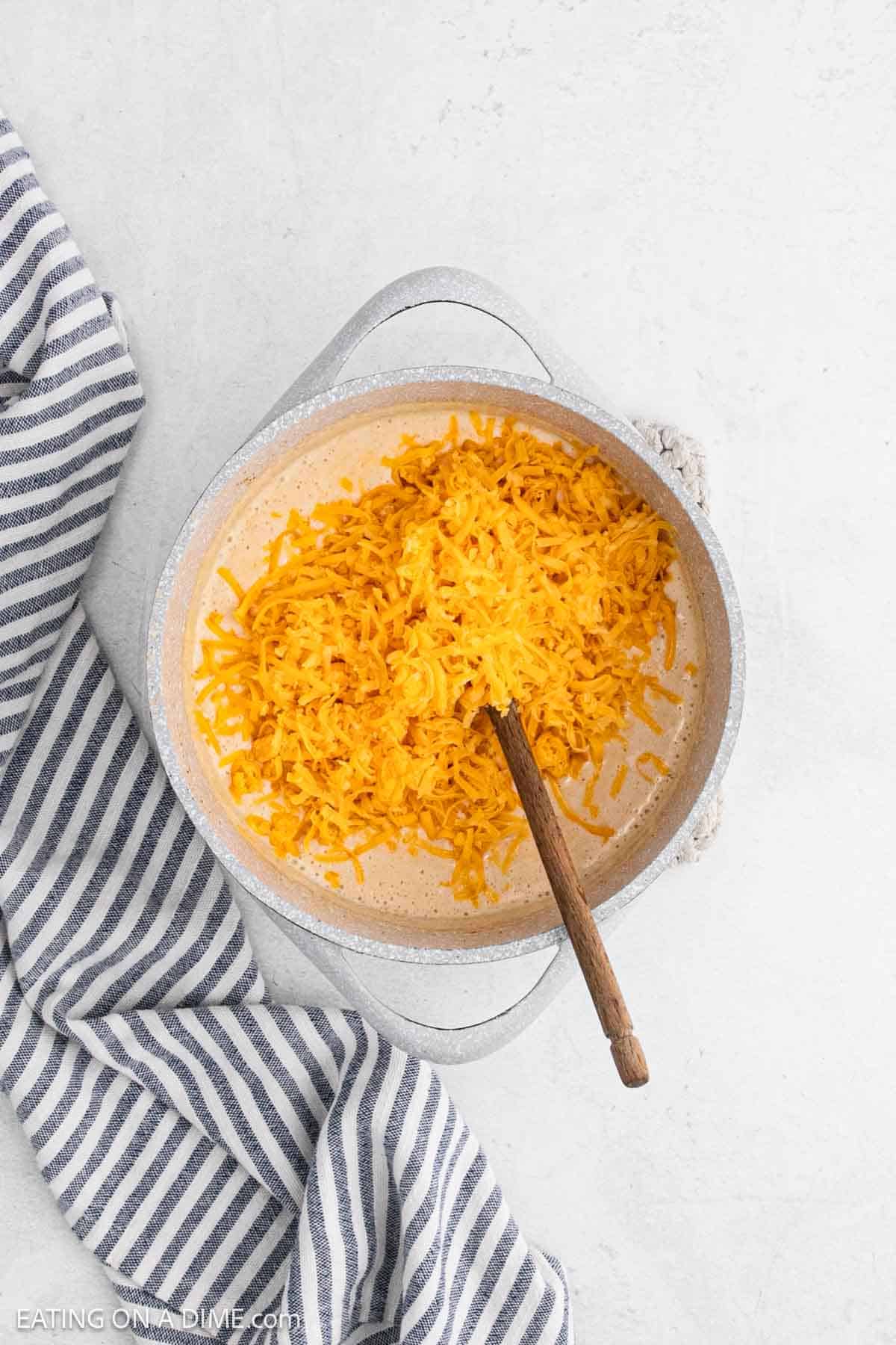 Shredded cheese added to the milk mixture in a large pot.