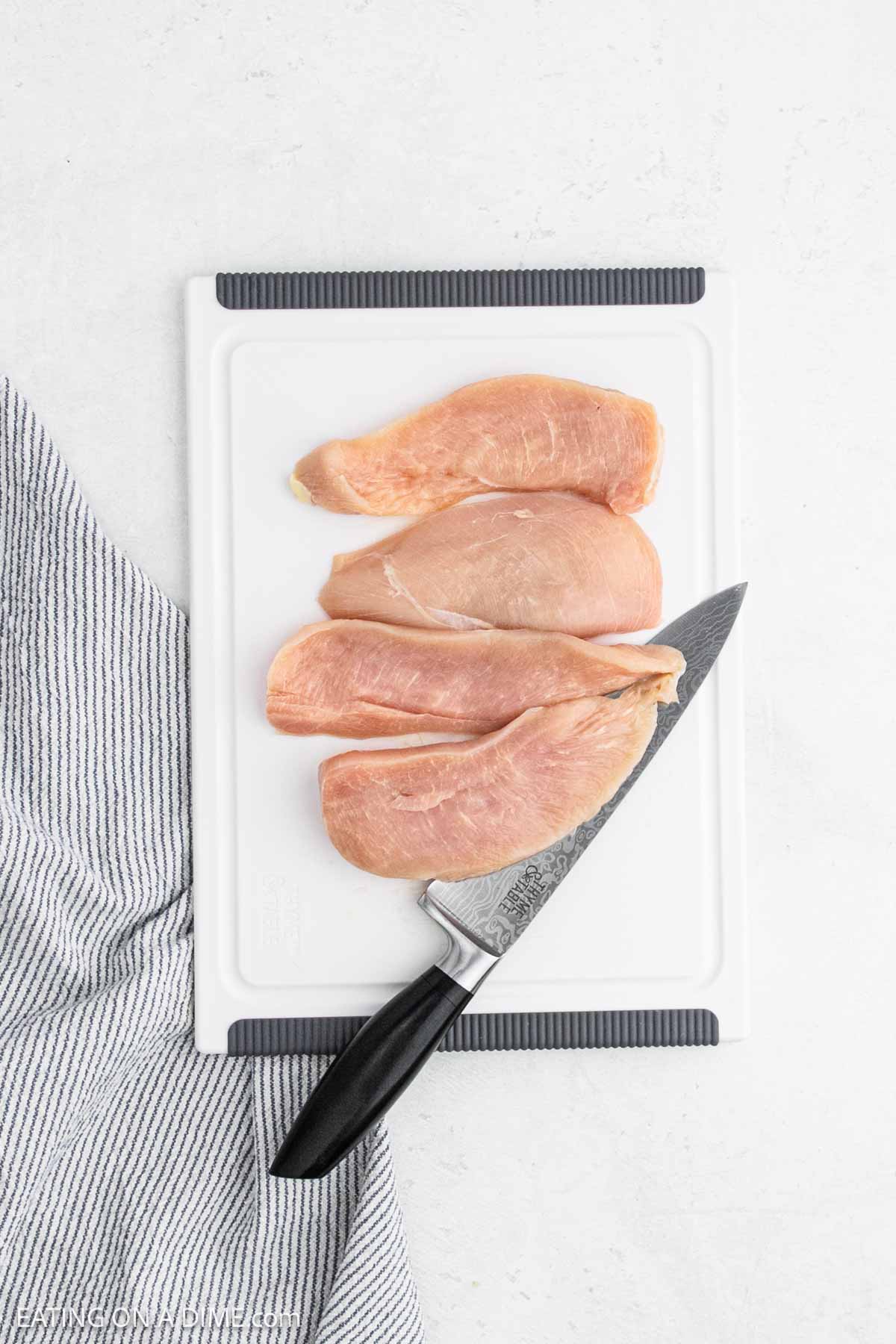 Slicing chicken breast with a knife on a cutting board.