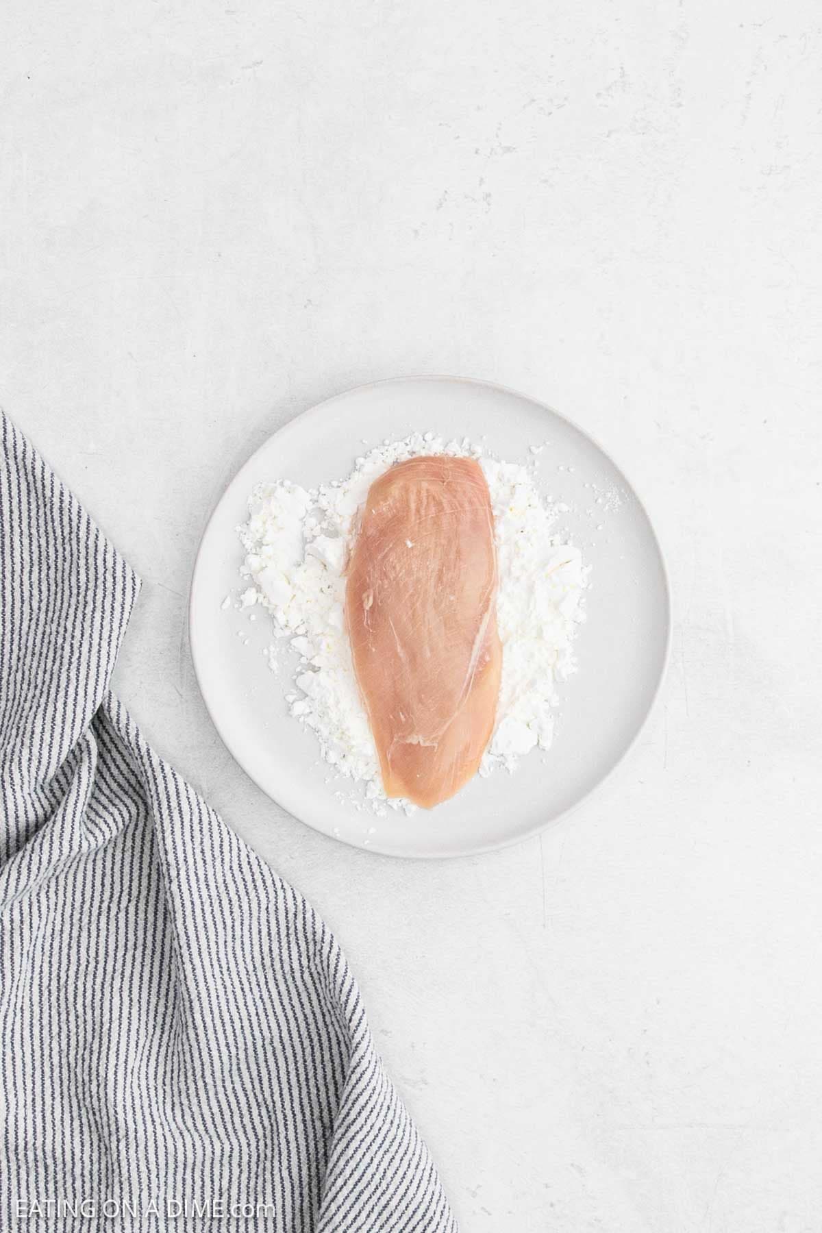 Placing chicken breast on a plate with cornstarch.