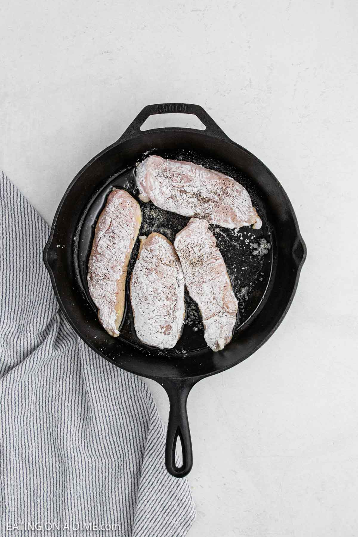Placing the chicken breast covered with cornstarch in a cast iron skillet.
