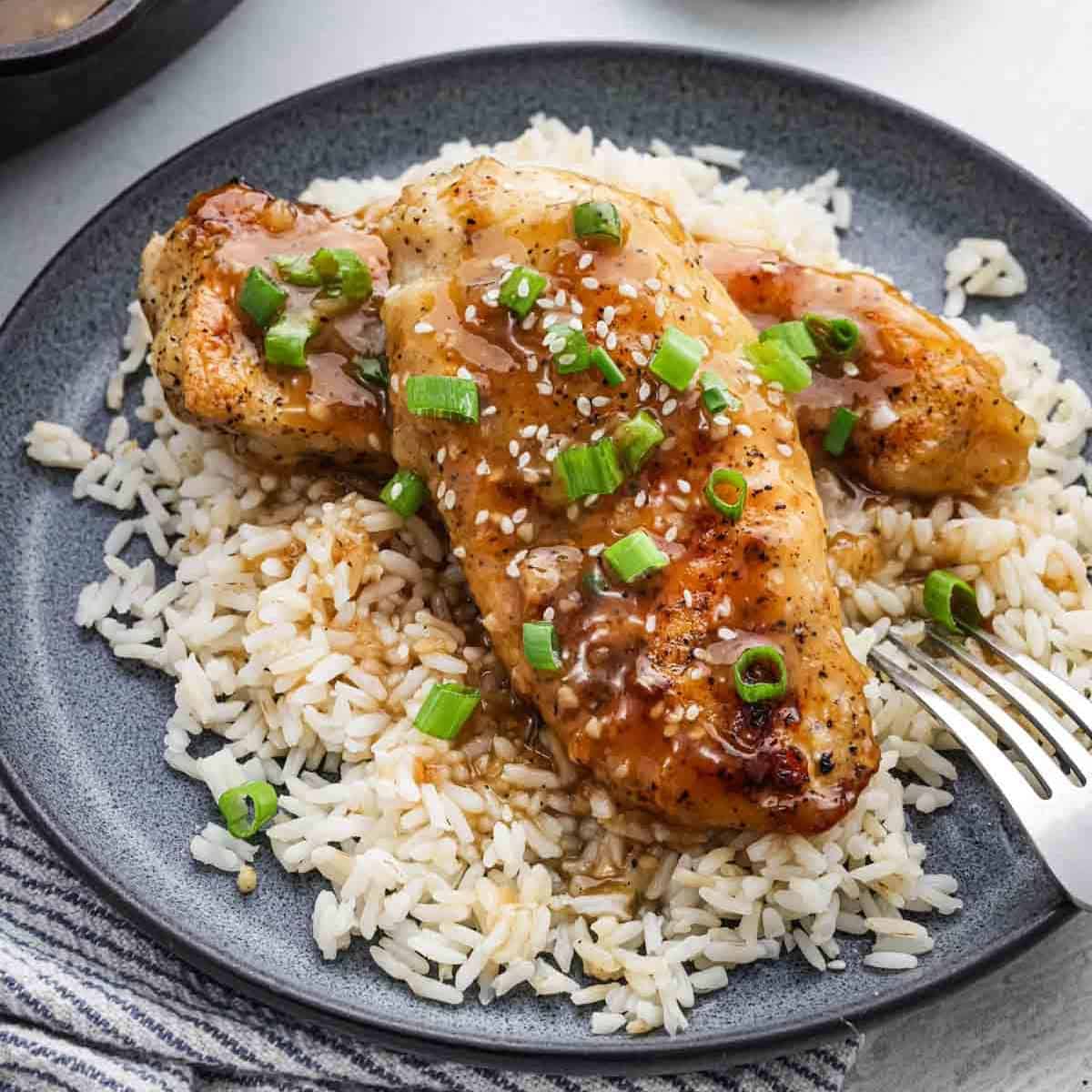 Honey chicken over rice on a plate topped with green onions and sesame seeds.