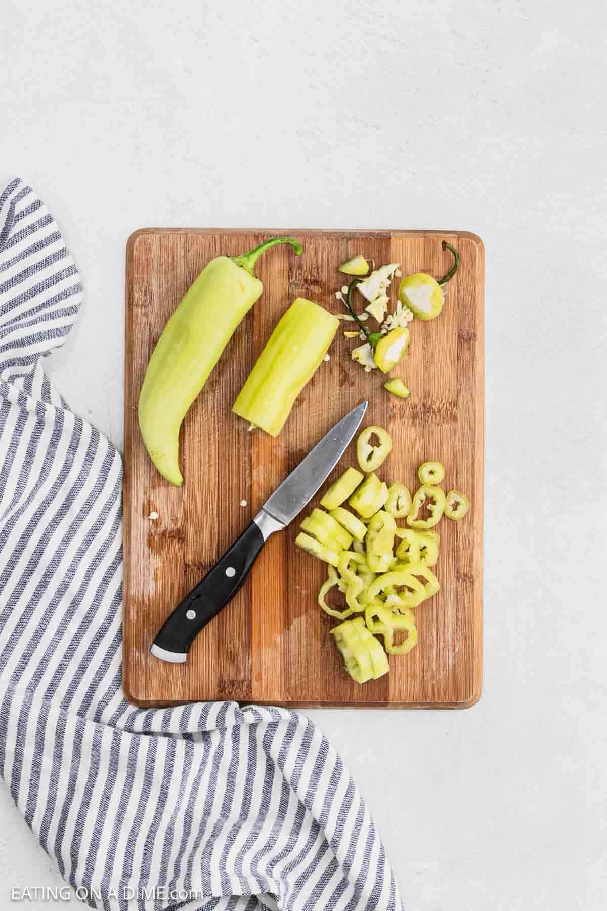 Slicing banana peppers on a cutting board with a knife.
