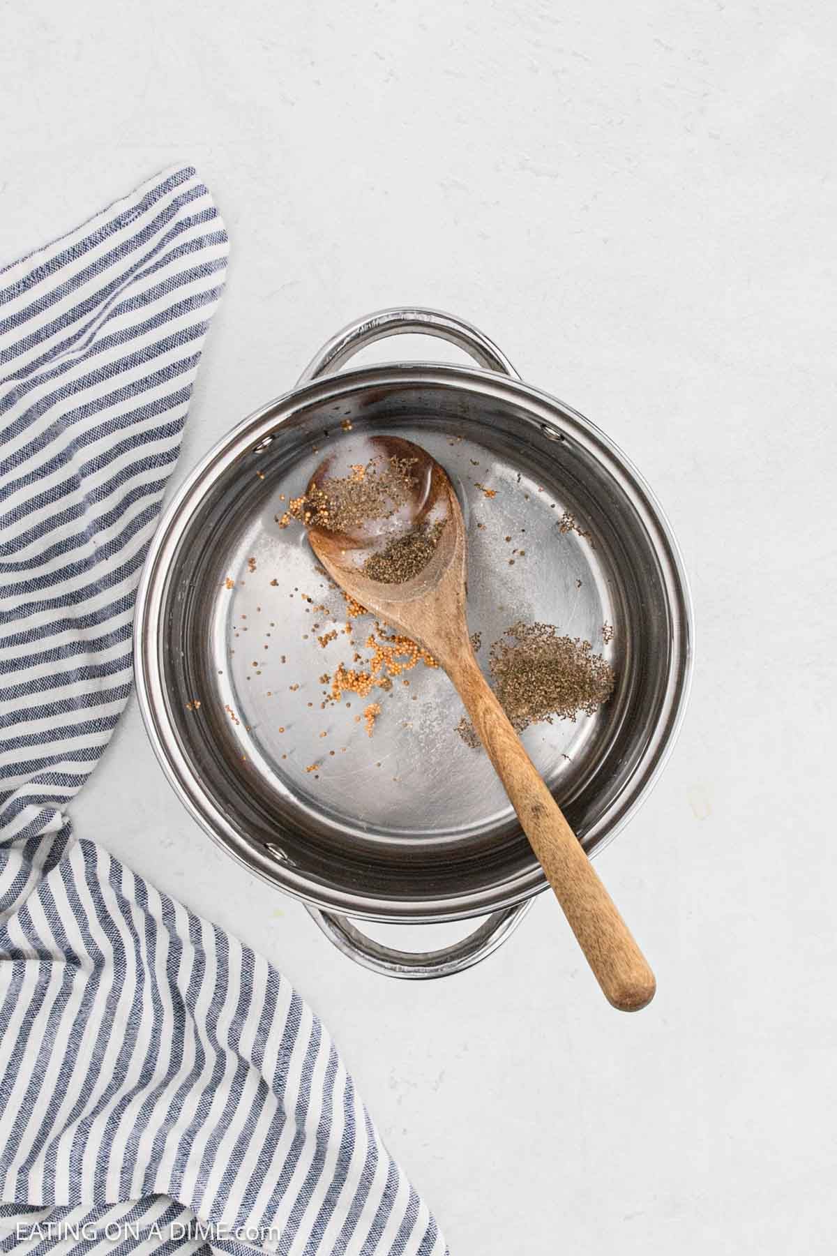 Spices and vinegar in a large pot with wooden spoon.