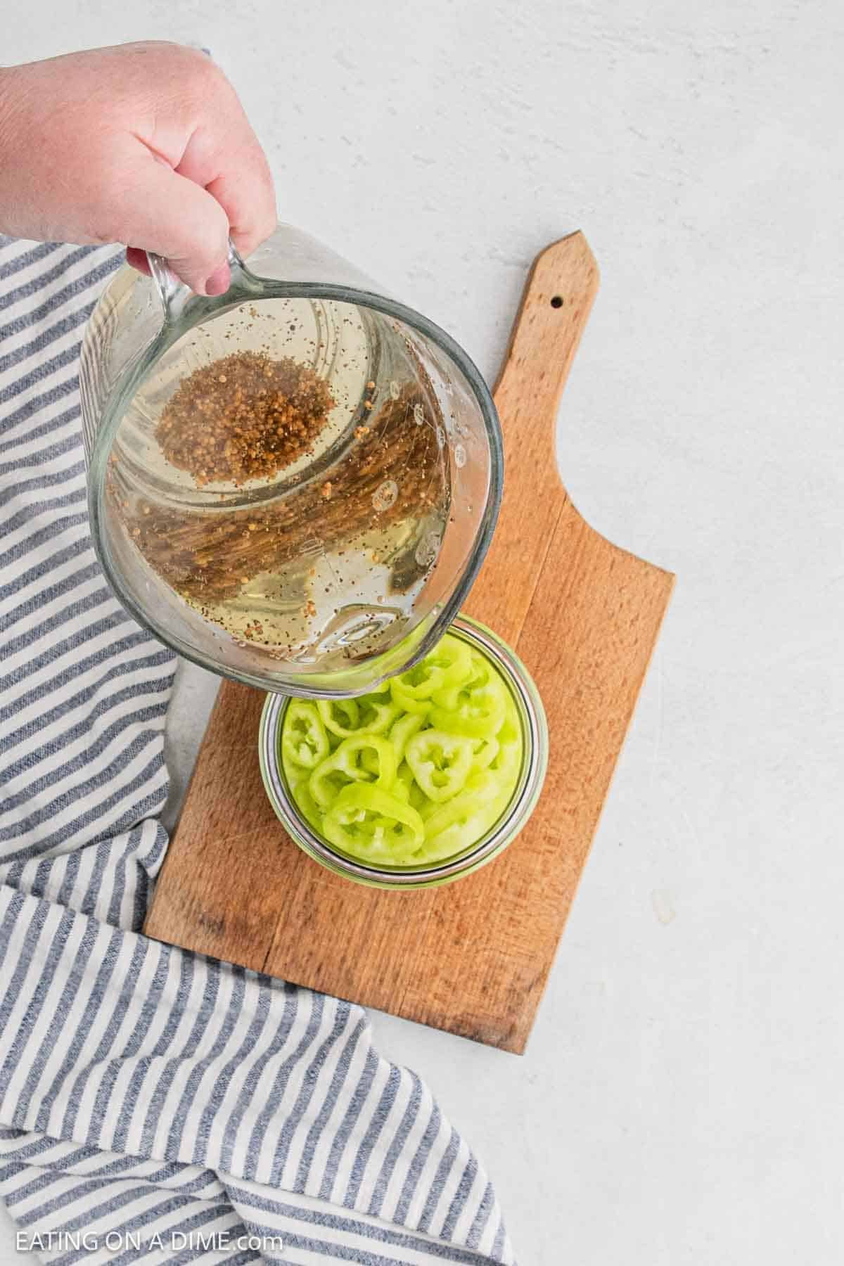 Pouring the vinegar mixture over the jar of the banana peppers.