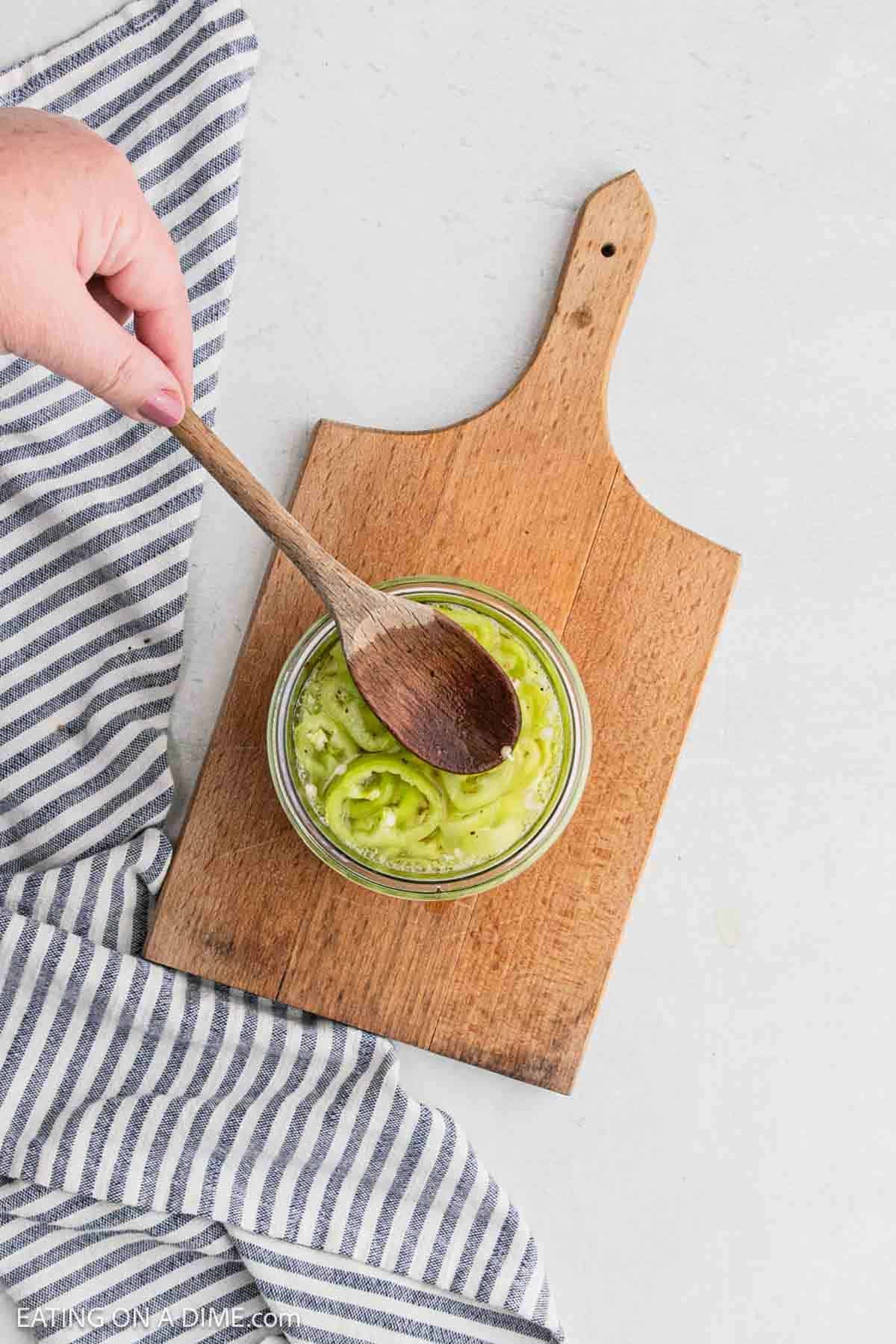 Wooden spoon pressing the banana peppers in the jar into the liquid.