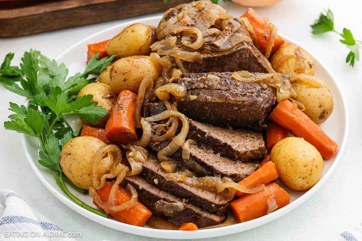 Sliced london broil on a white plate with a side of cooked potatoes and carrots.