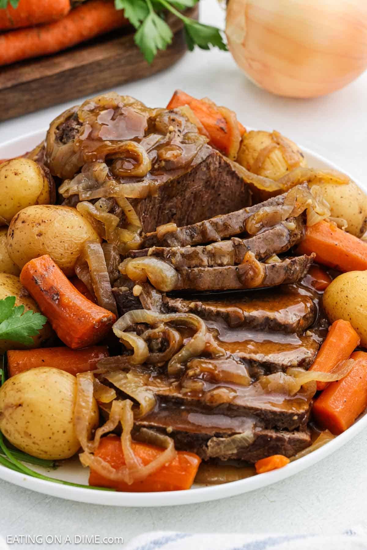 Sliced london broil topped with gravy with a side of cooked potatoes and carrots on a platter.
