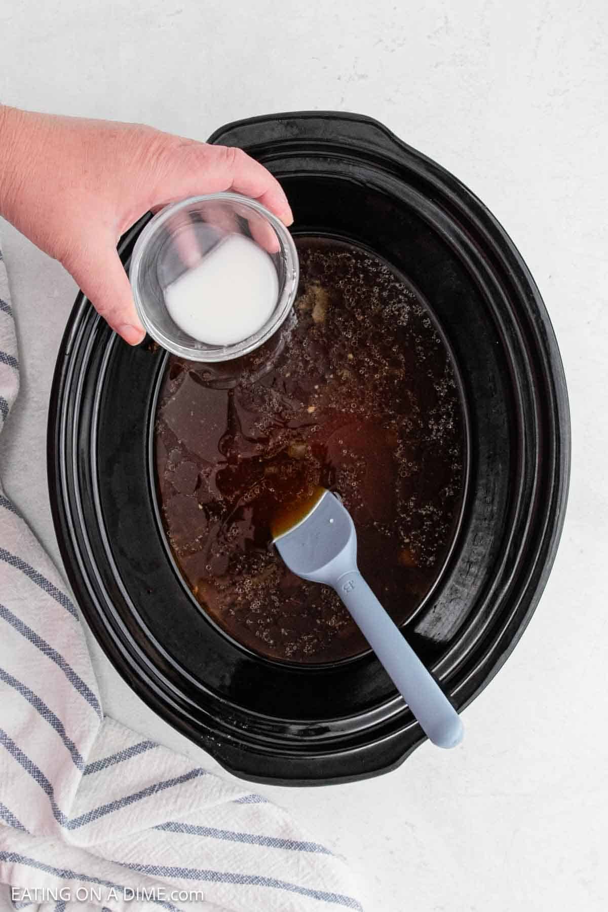 Pouring the cornstarch mixture into the gravy in the slow cooker.