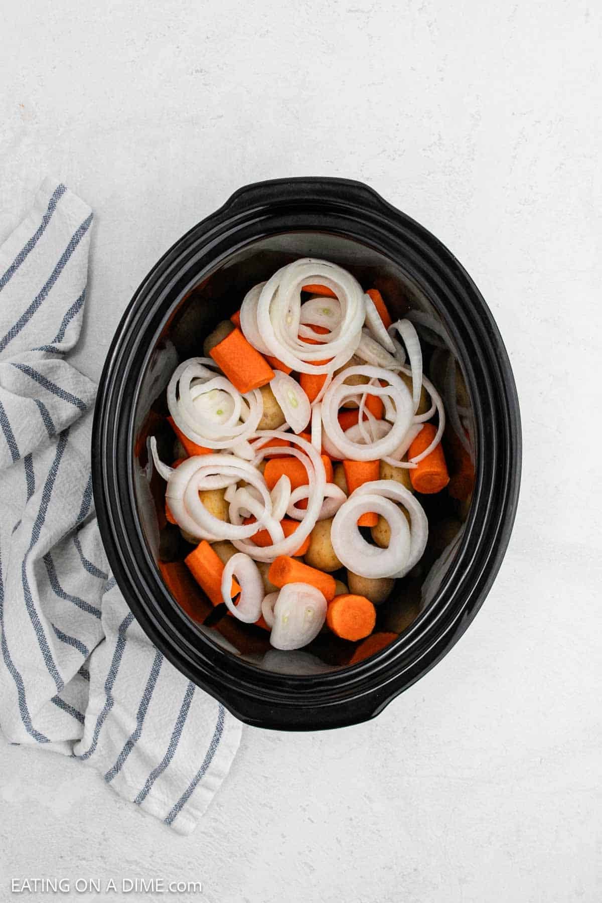 Chopped carrots and onions placed in the slow cooker.