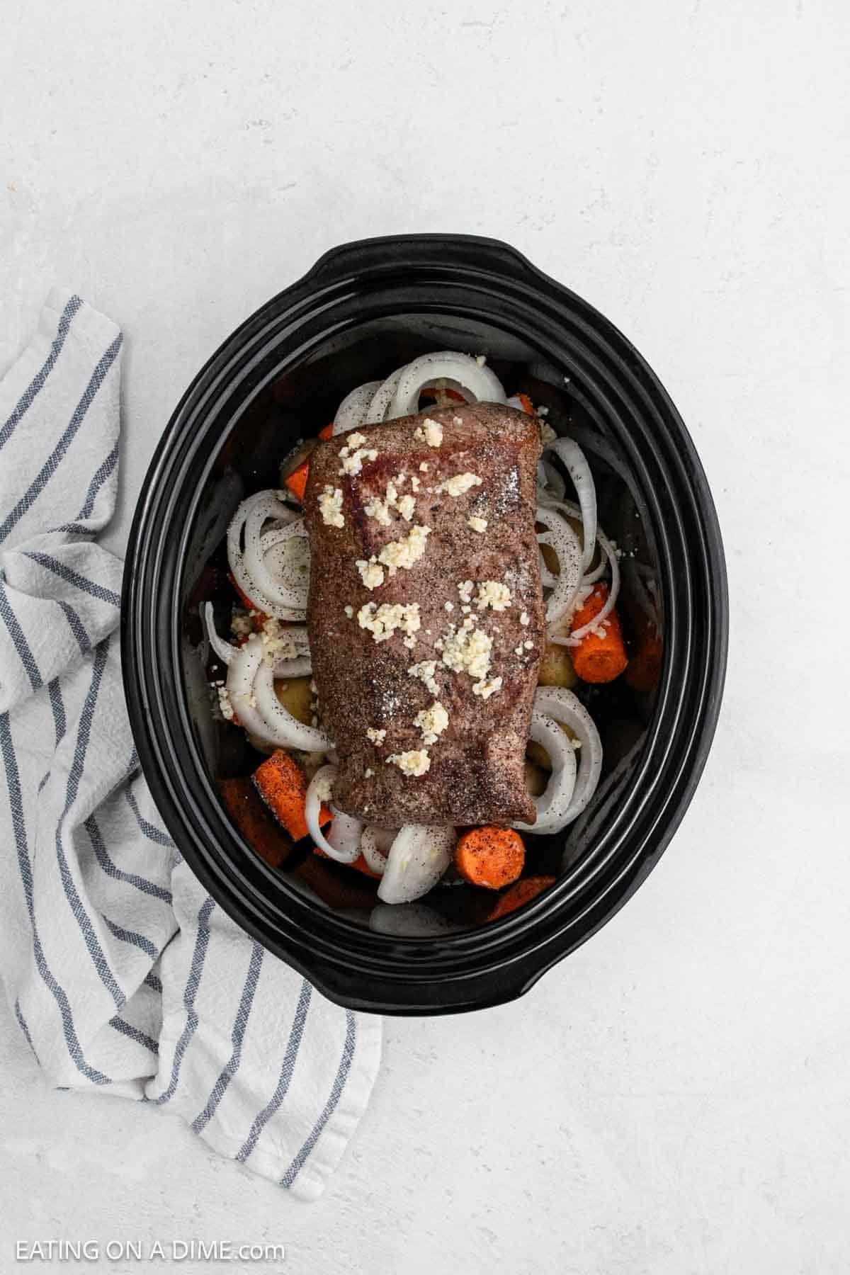 Seared london broil placed on top of the chopped onions and carrots in the slow cooker.