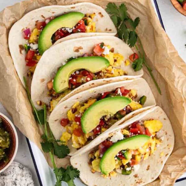 Breakfast tacos topped with slice avocado on a tray.