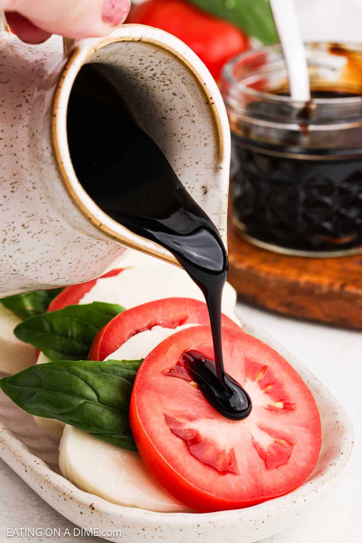 Drizzling the glaze over the fresh tomato and mozzarella salad on a platter.