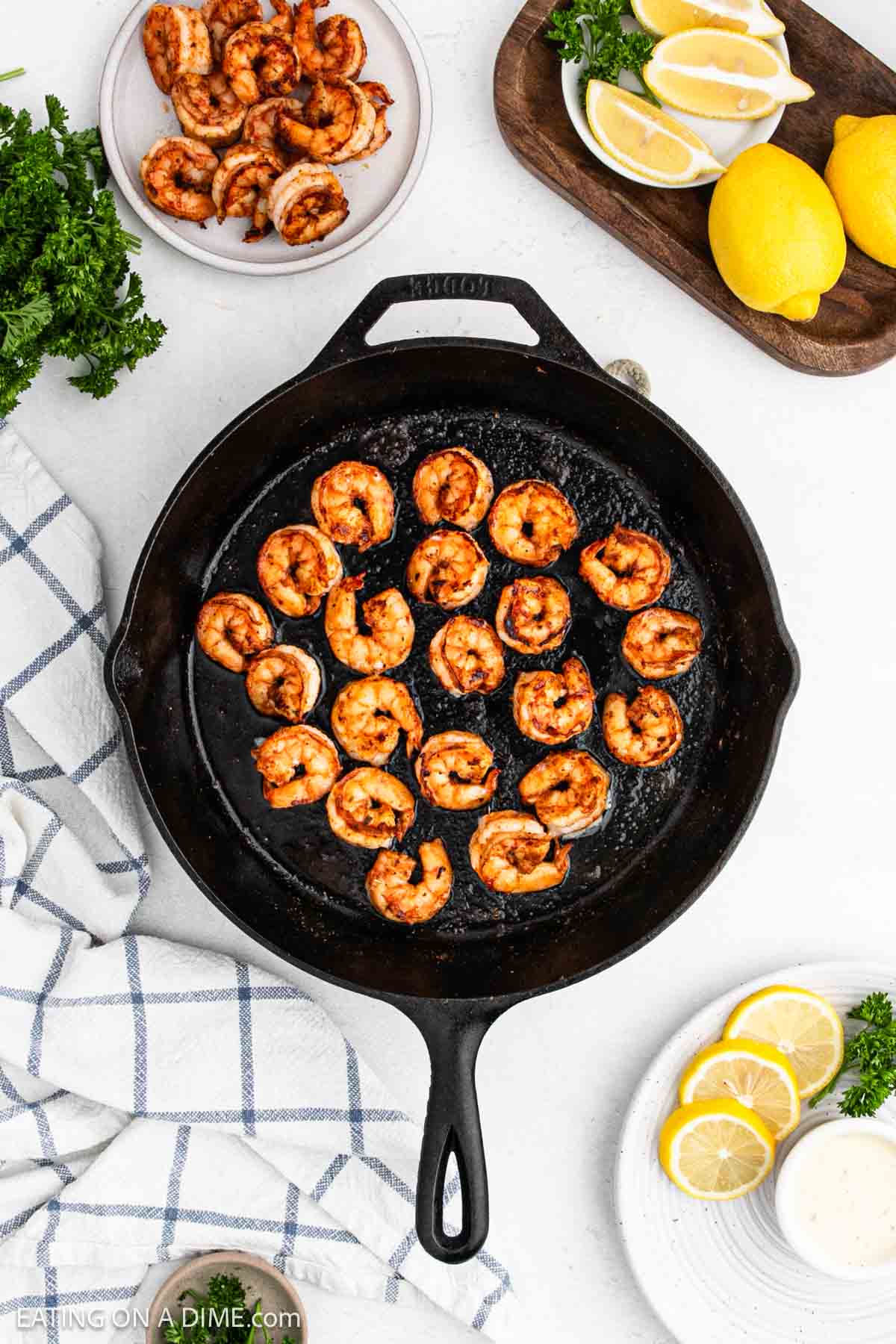 Cooked shrimp in a cast iron skillet with a wooden platter of lemon wedges on the side.