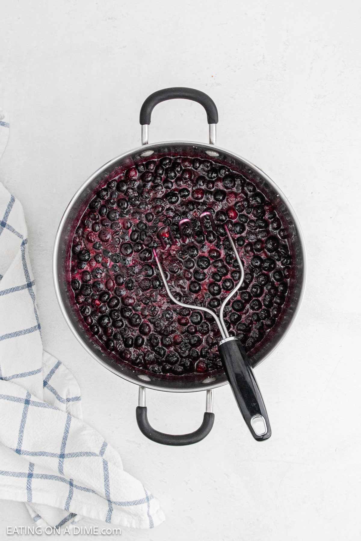 Smashing cooked blueberries in a large pot.