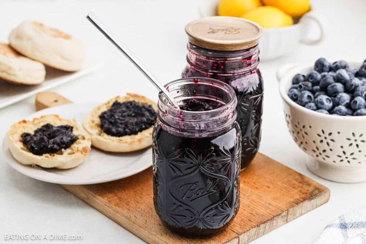 Blueberry Jam in mason jars with a biscuit topped with the jam on a plate.