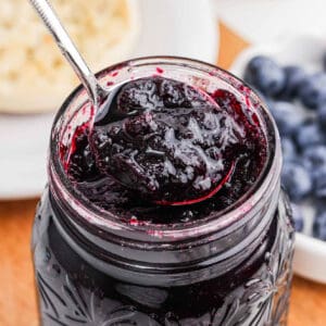 Blueberry Jam in a jar with a serving on a spoon.