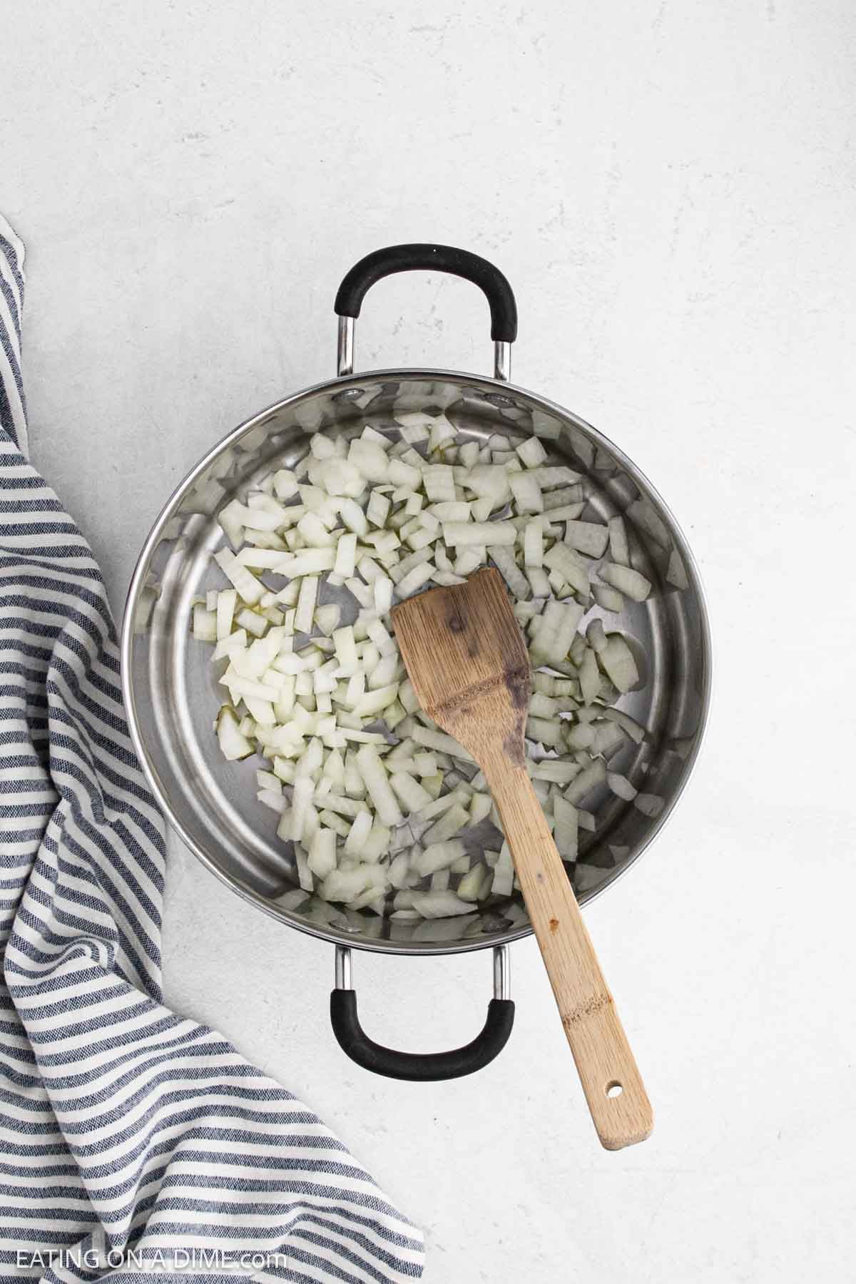 Diced onions in a large pot with a wooden spoon.