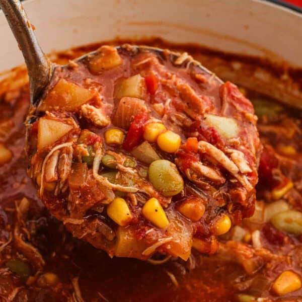 Brunswick Stew serving in a ladle over a large pot of stew.