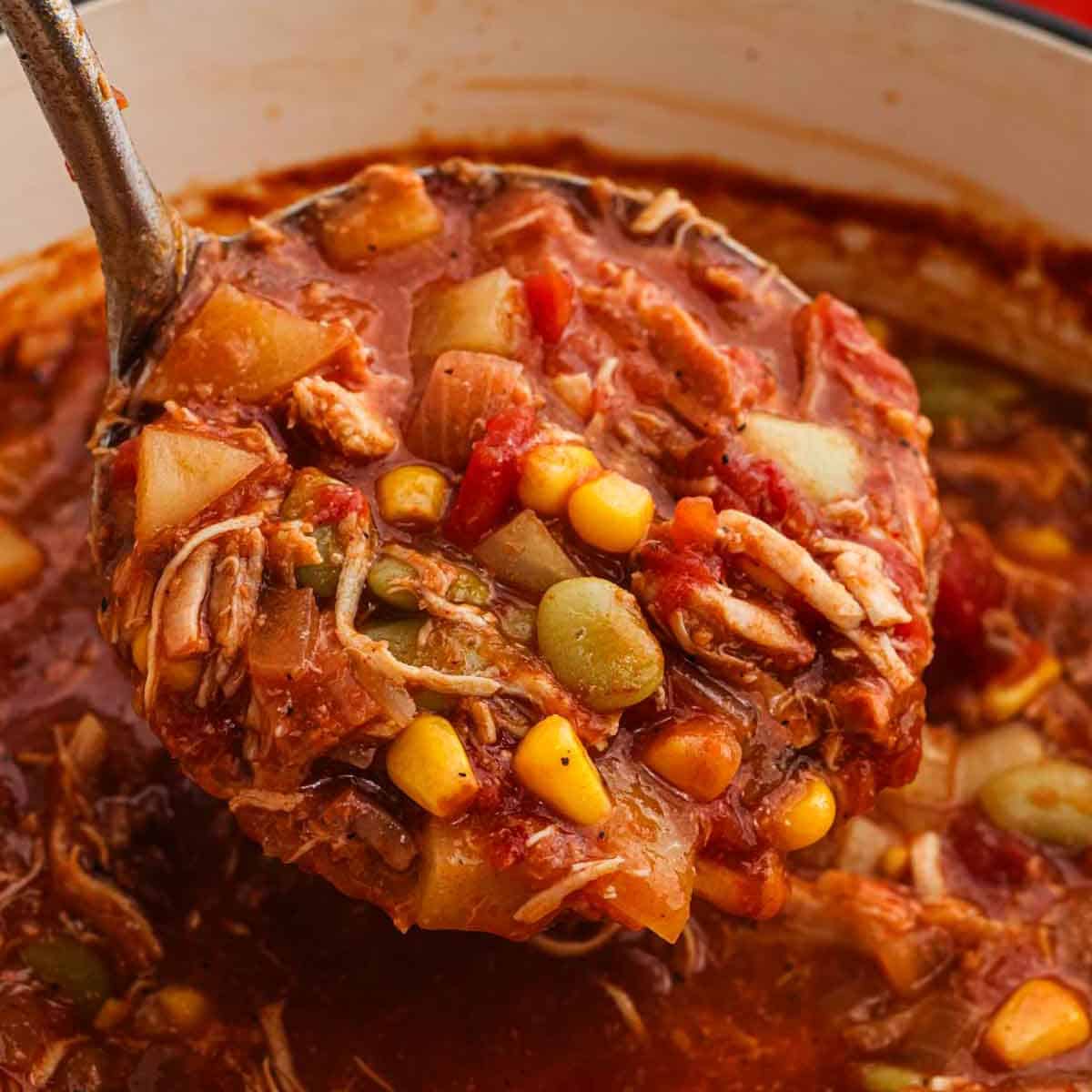 Brunswick Stew serving in a ladle over a large pot of stew.