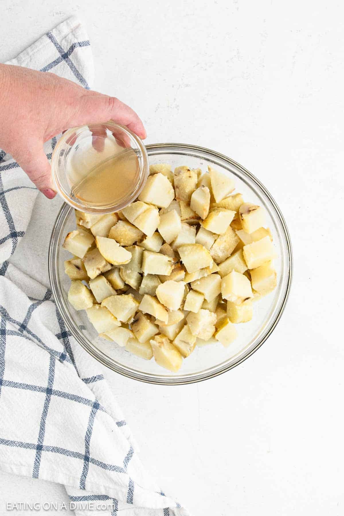 Pouring apple cider vinegar over the diced baked potatoes in a bowl.