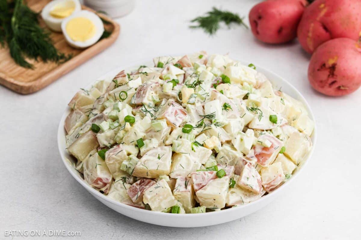 Potato salad in a bowl topped with green onions and fresh dill.