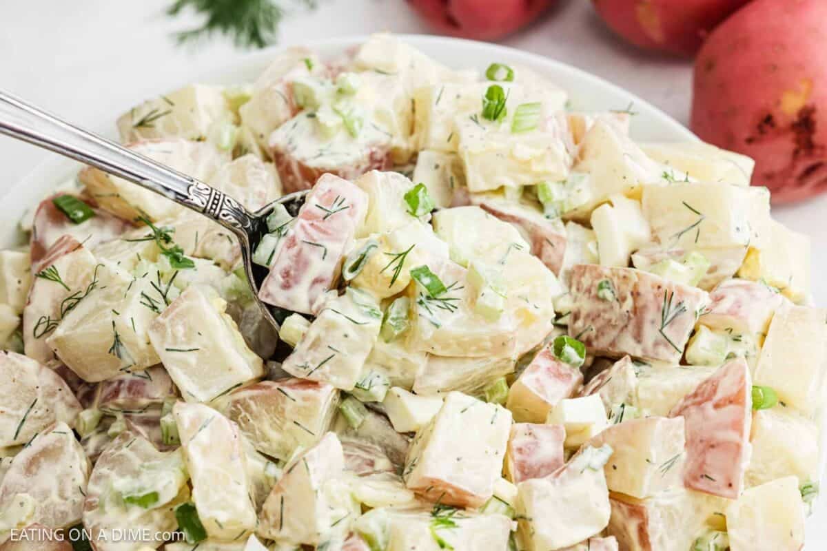Red potato salad in a bowl with a serving on a spoon. 