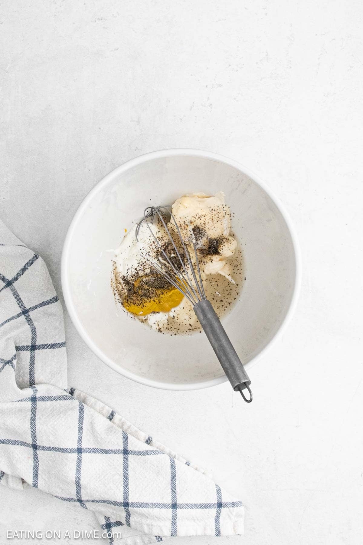 Combining the mayonnaise, sour cream, white wine vinegar, yellow mustard, salt, and pepper in a bowl with a whisk.