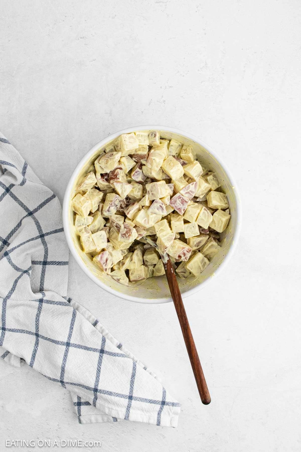 Diced red potatoes combined with the dressing in a bowl with a wooden spoon.