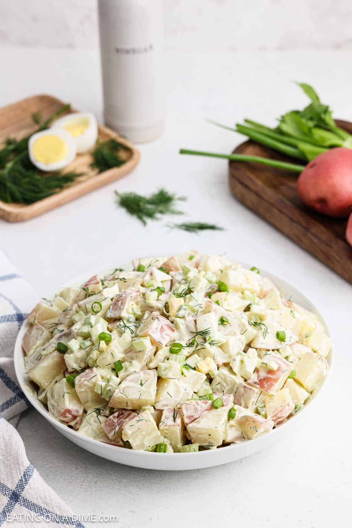 Potato salad in a bowl topped with fresh dill and green onions.