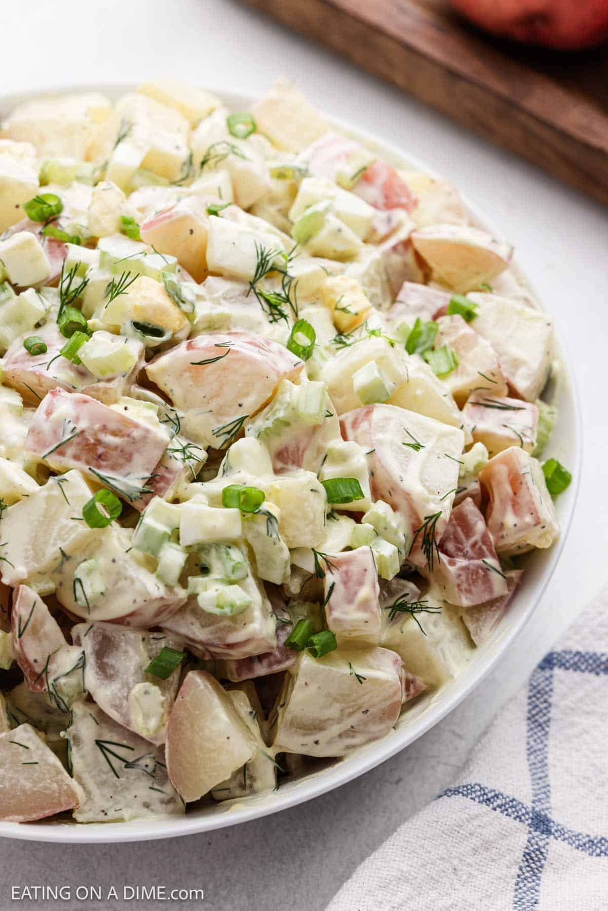 Finished potato salad recipe in a bowl topped with green onions and fresh dill.