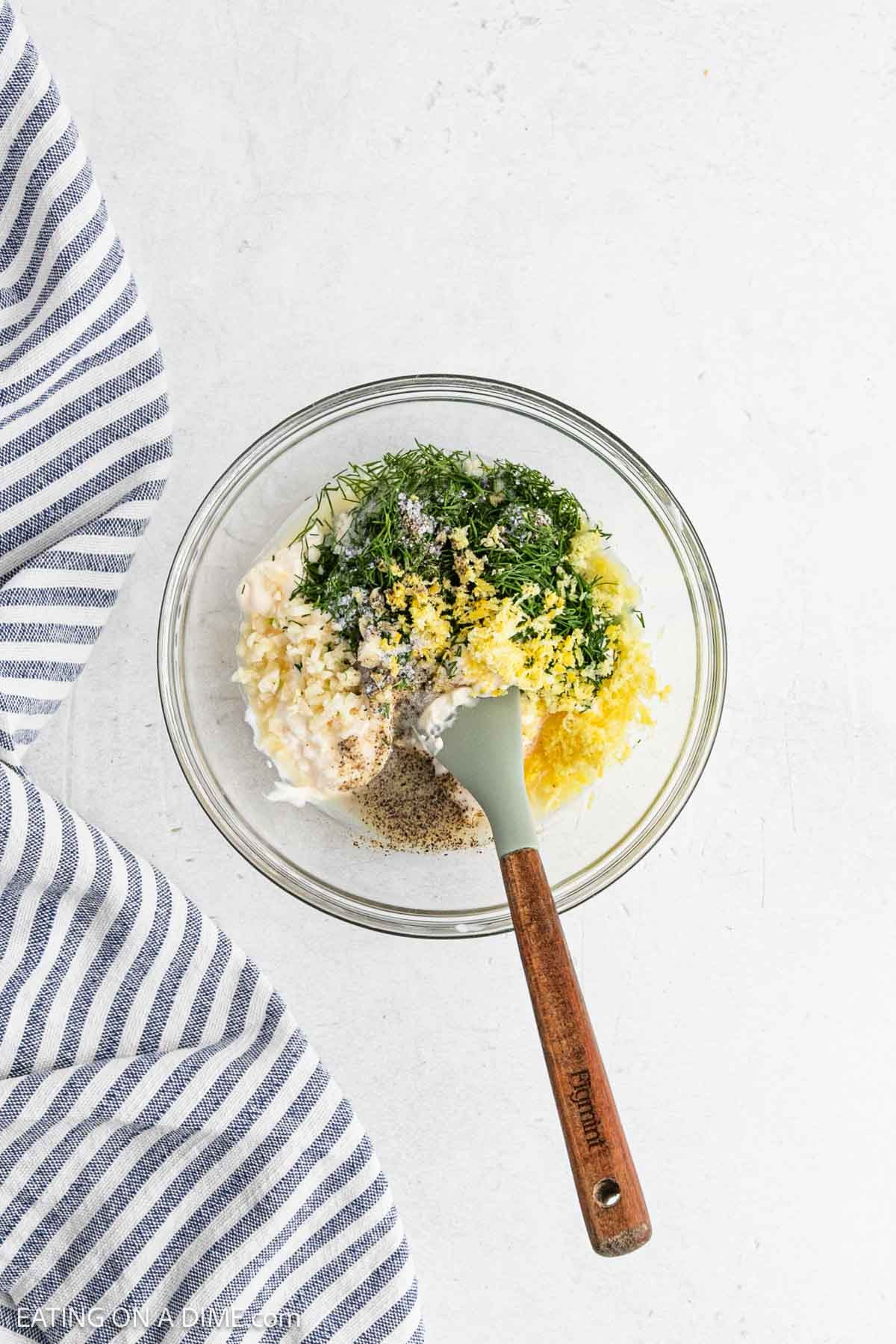 Combining the lemon dill dressing in a bowl with a spatula.